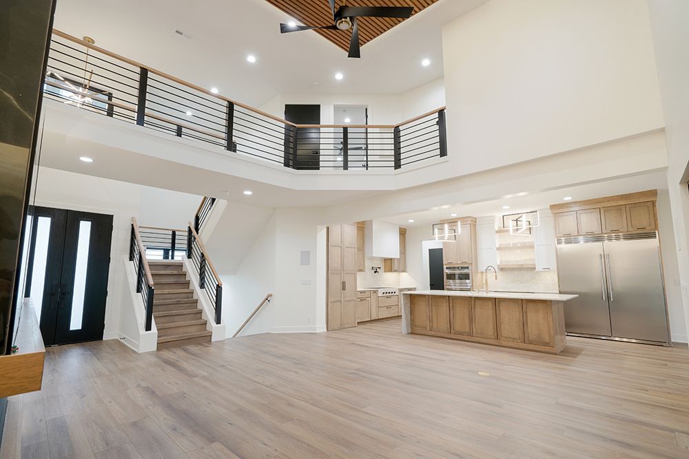 Open-concept home interior with a staircase, kitchen, and balcony. Wooden floors and cabinets, white walls.