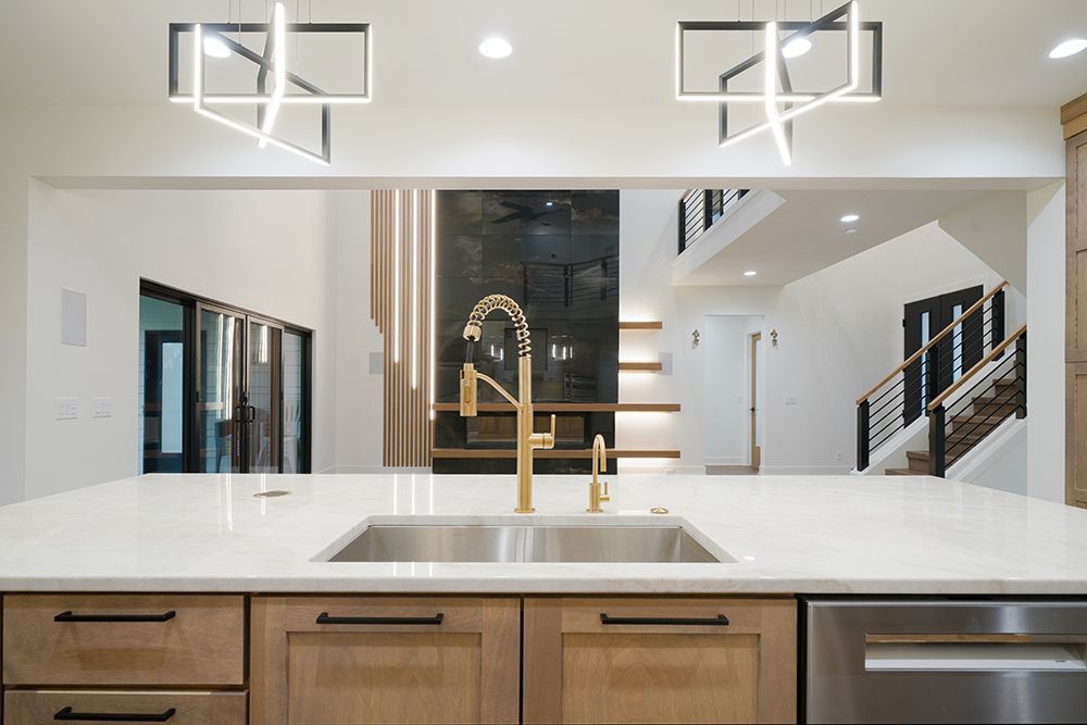 Kitchen with gold faucet, light wood cabinets, and modern light fixtures. Open to living area.