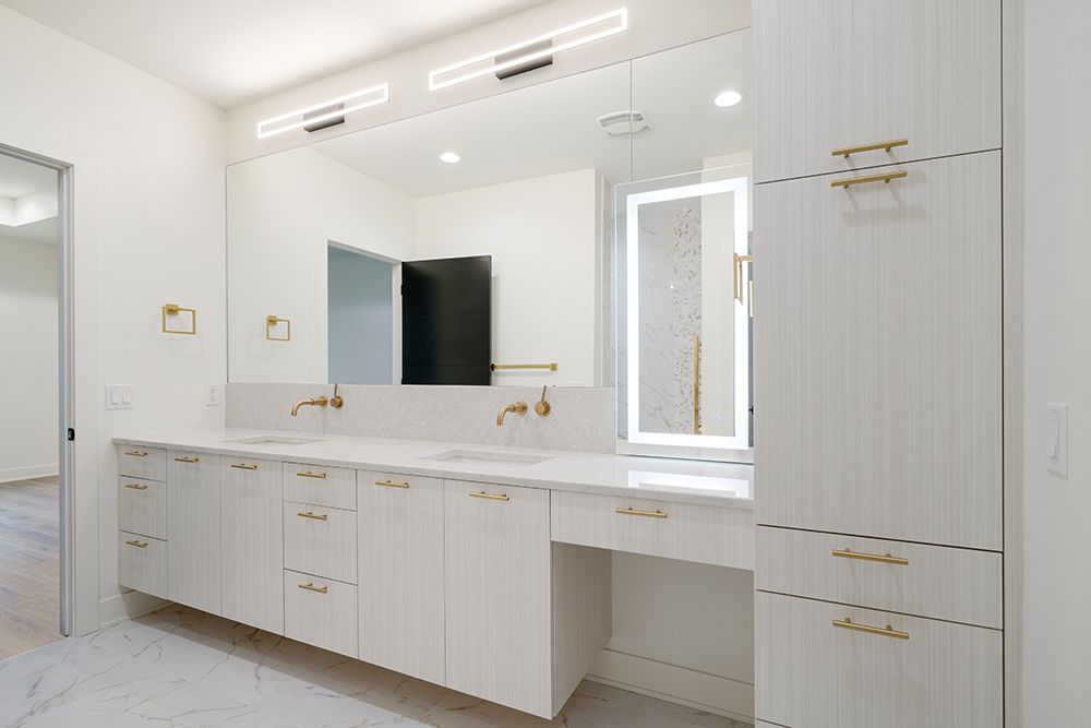 Modern bathroom with white cabinets, gold fixtures, marble countertop, and large mirror.