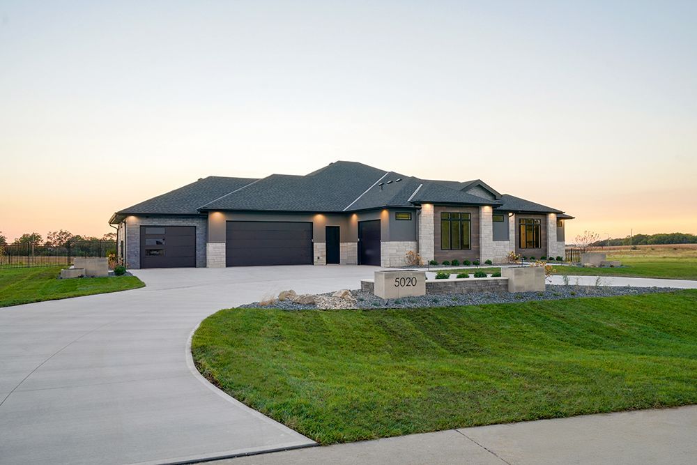 Modern ranch-style home with gray siding, three-car garage, and concrete driveway, set against an evening sky.