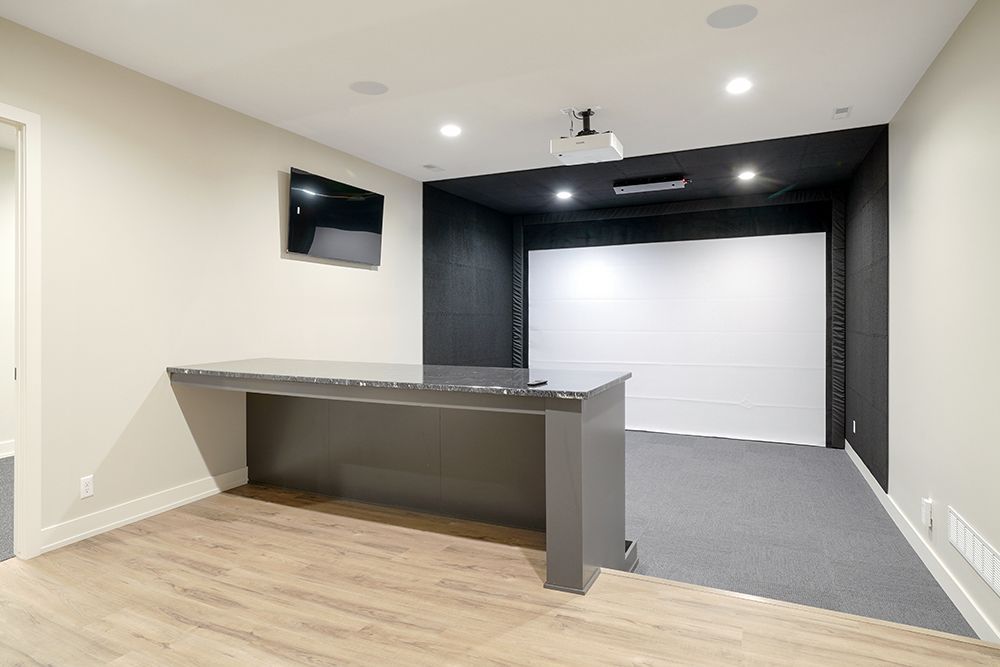 Home theater room with projector screen, wall-mounted TV, bar, and gray carpet.