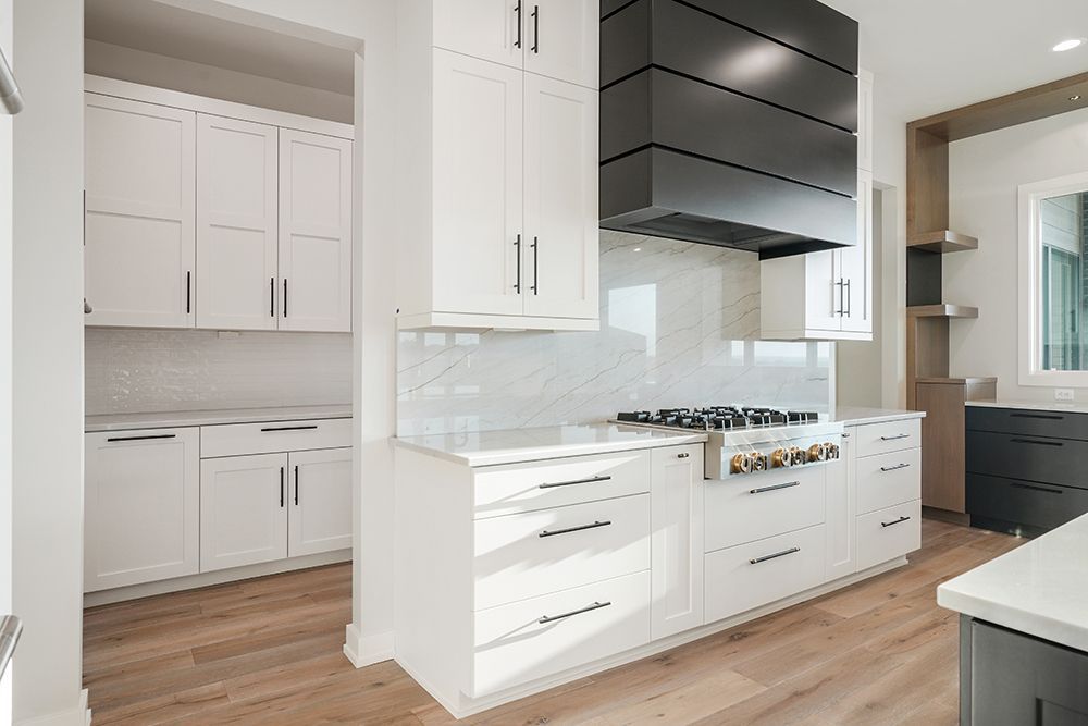 Modern kitchen with white cabinets, wood floors, and a black range hood.
