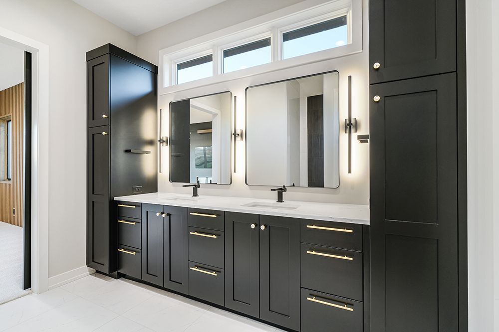 Black bathroom vanity with two mirrors, gold hardware, and two tall storage cabinets.