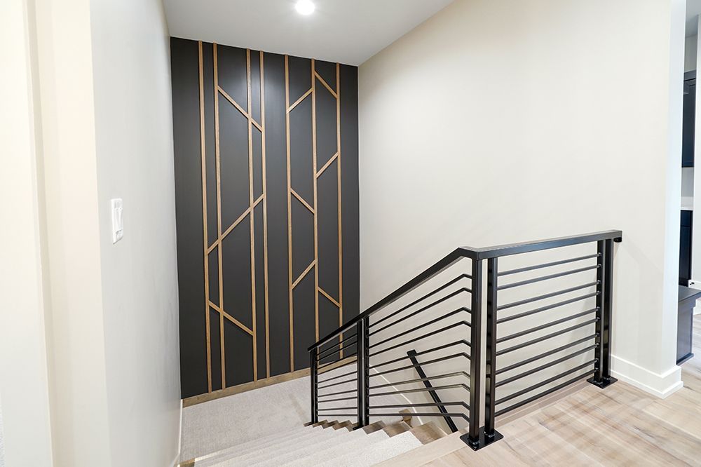 Staircase with black metal railing and geometric wood accent wall. Light beige walls, wood steps.
