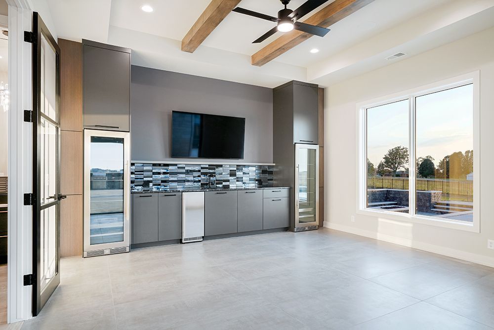 Modern, empty room with grey cabinets, TV, and large windows. Includes wooden beams and a ceiling fan.