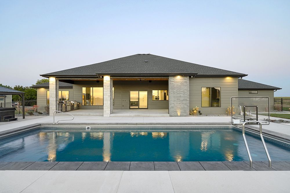 Backyard view: a house with a pool. Grey siding, dark roof, rectangular pool with ladder.
