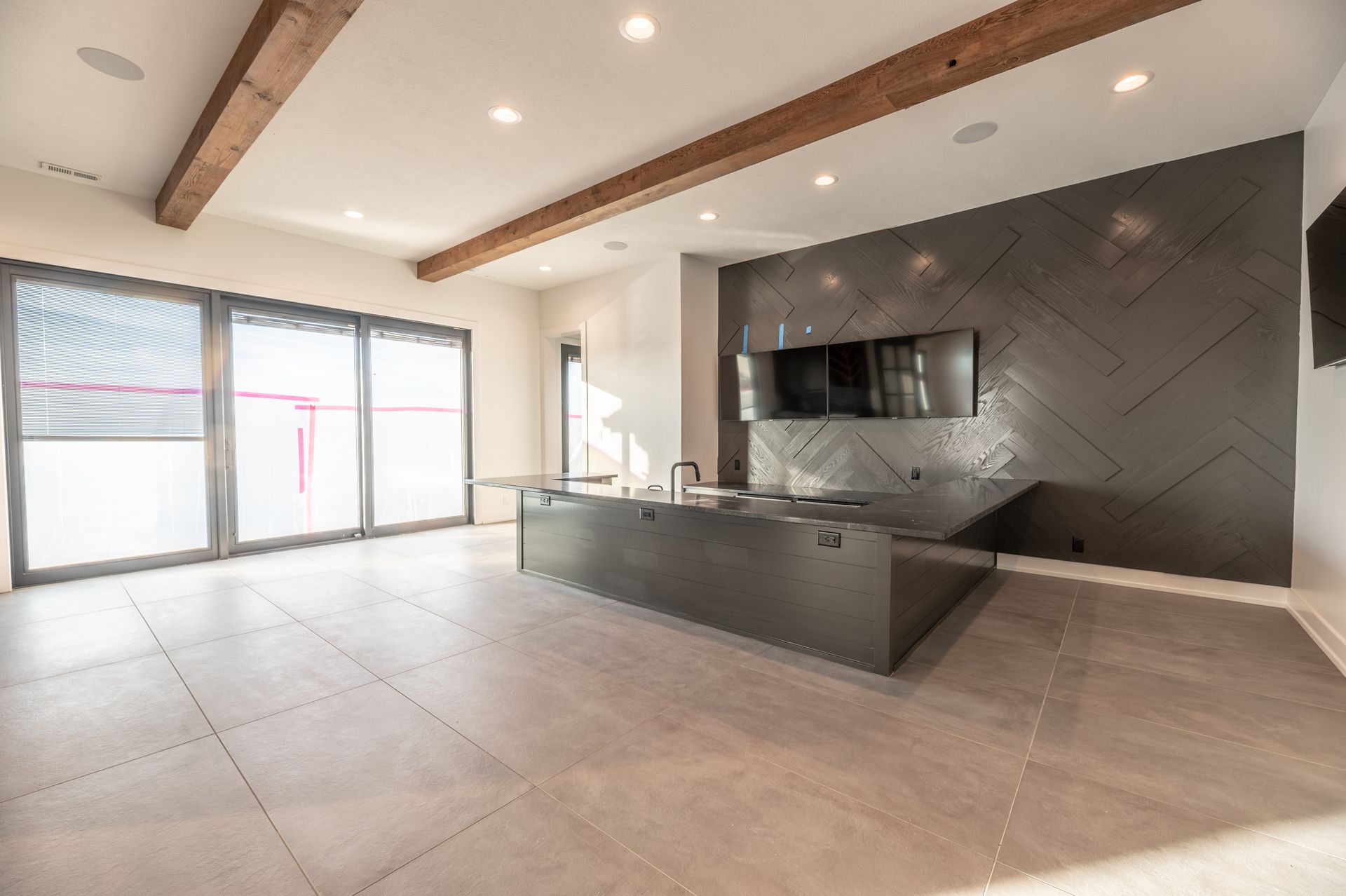 Modern entertainment room with large sliding doors, dark accent wall with TVs, and a gray island.