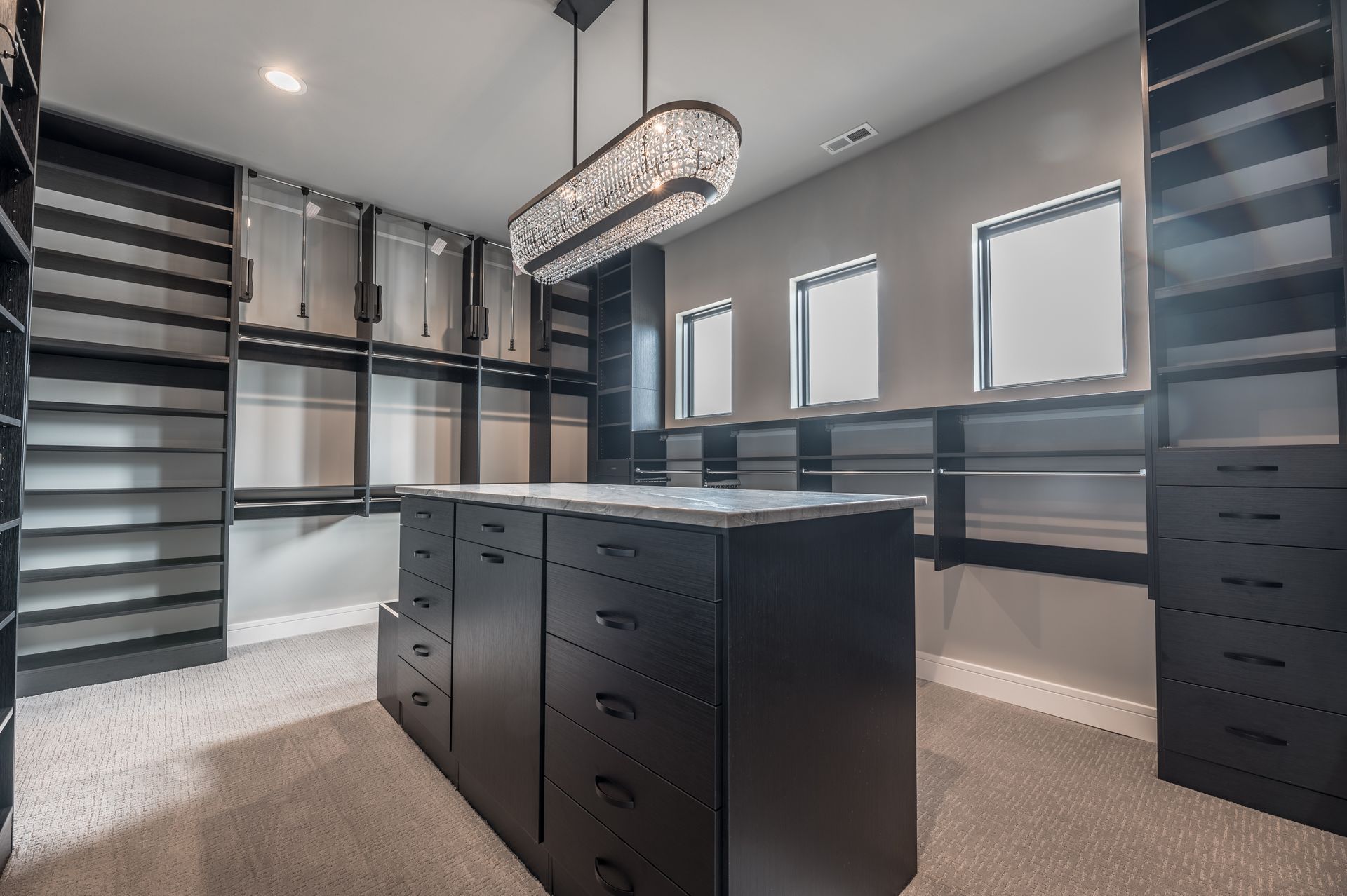 Walk-in closet with dark shelves, drawers, and a central island. A decorative light fixture hangs from the ceiling.