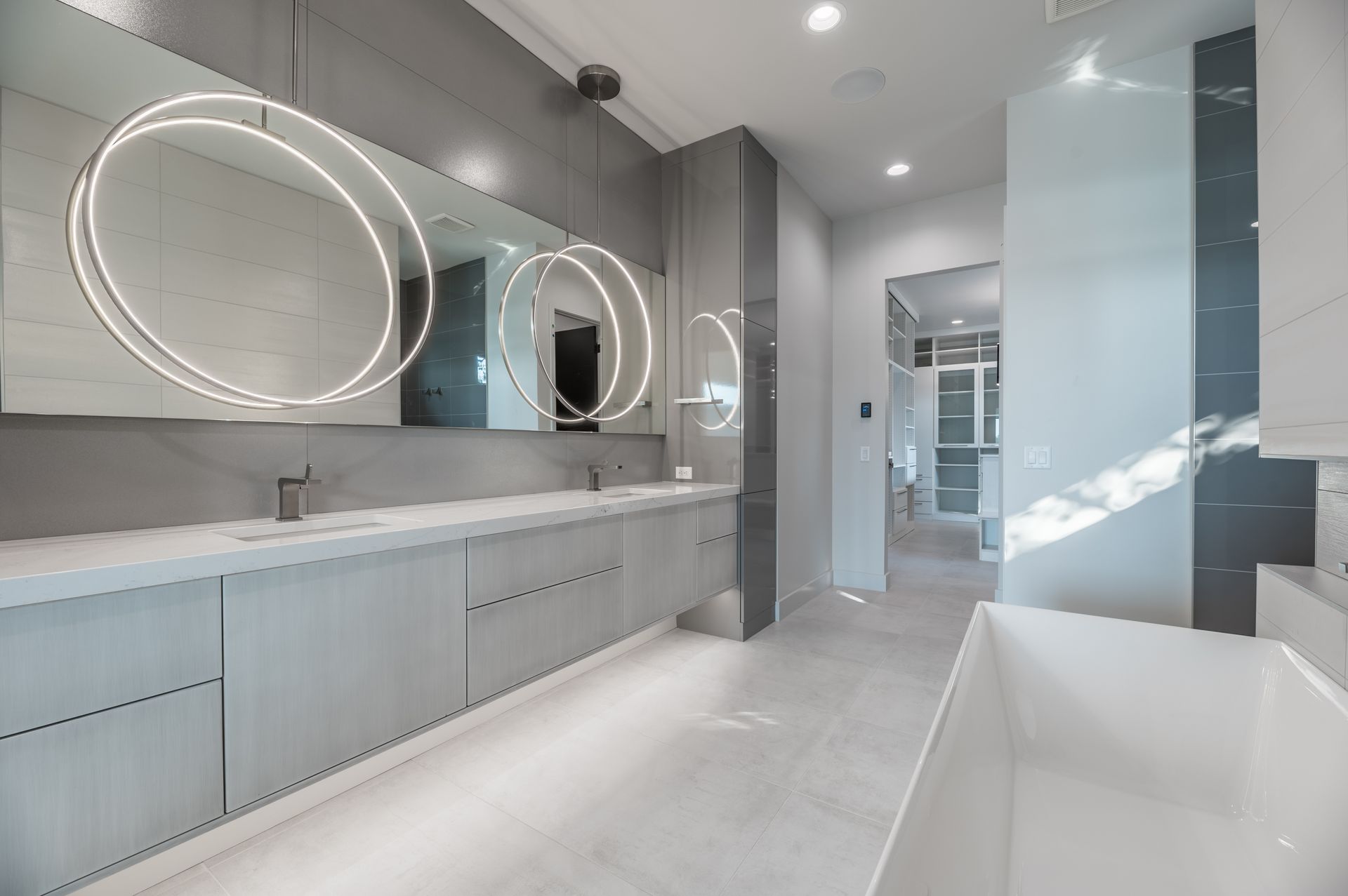 Modern gray and white bathroom with long vanity, circular mirrors, and tub.
