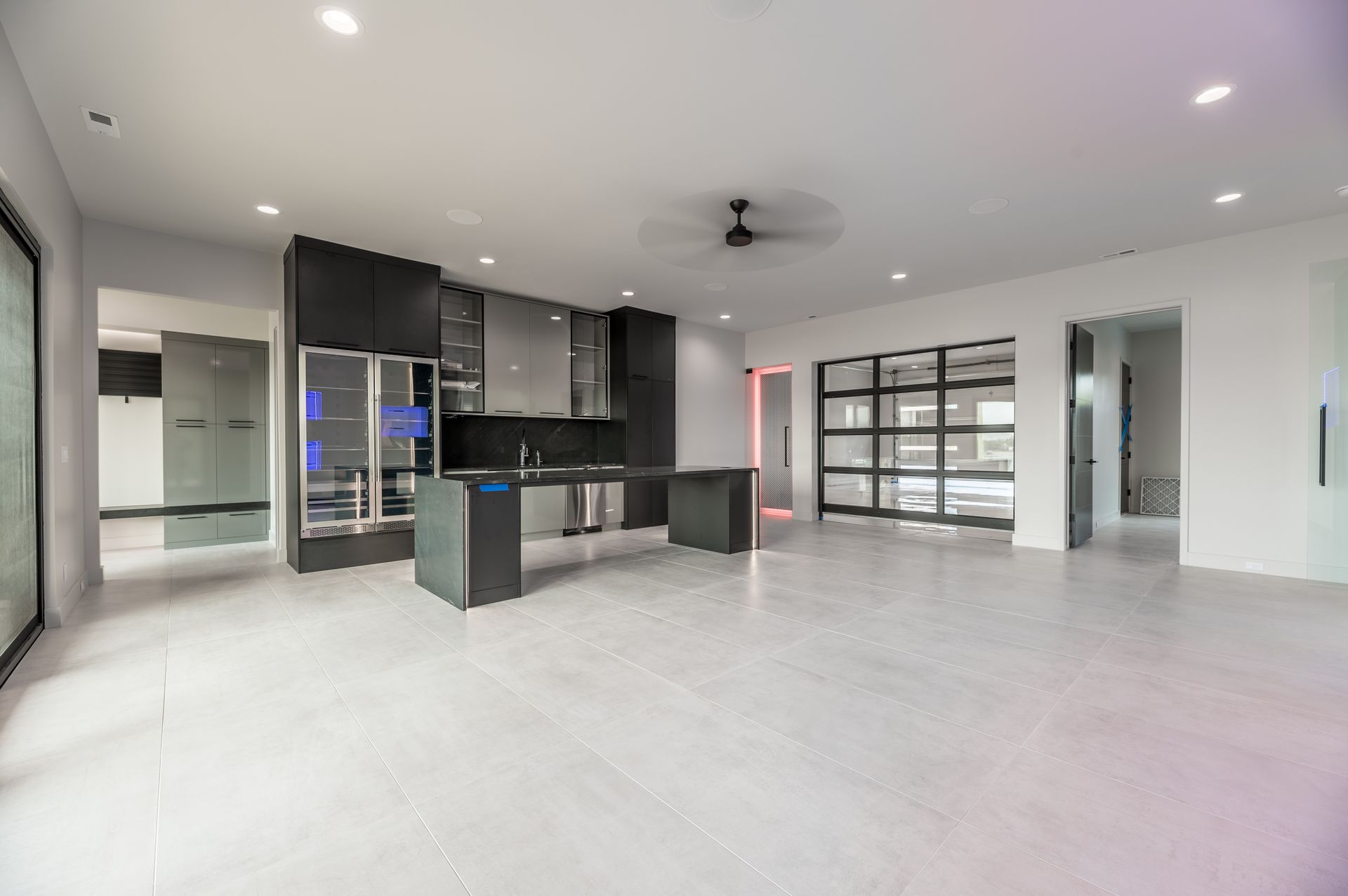 Modern open-plan kitchen with gray cabinets and island, light floors, and a glass-paneled garage door.