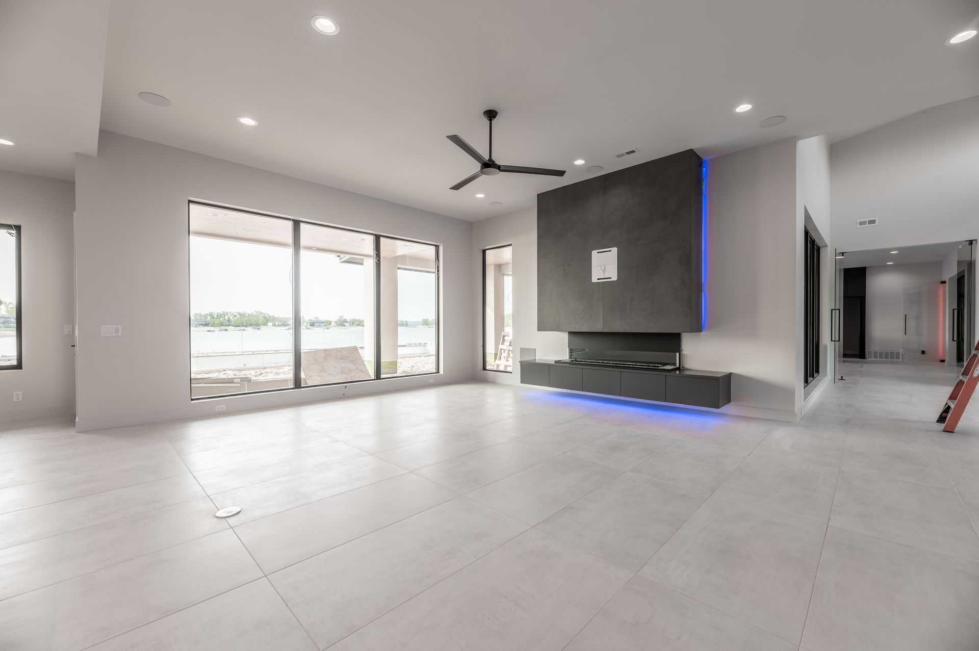 Empty modern living room with large windows, fireplace, and gray floors.