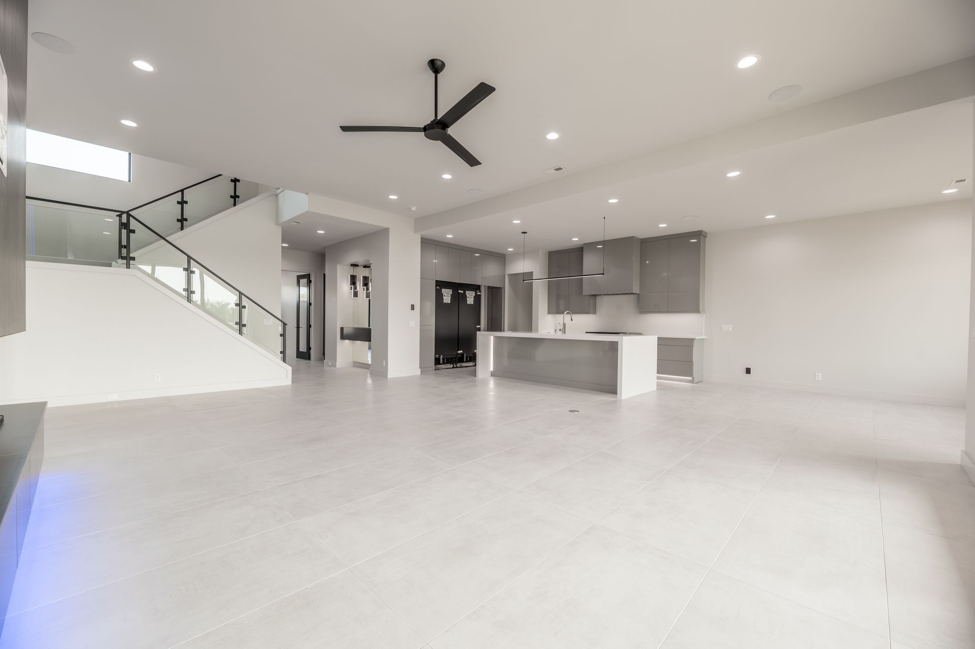 Modern, open-concept living space with a white tile floor, kitchen, and staircase with a black ceiling fan.