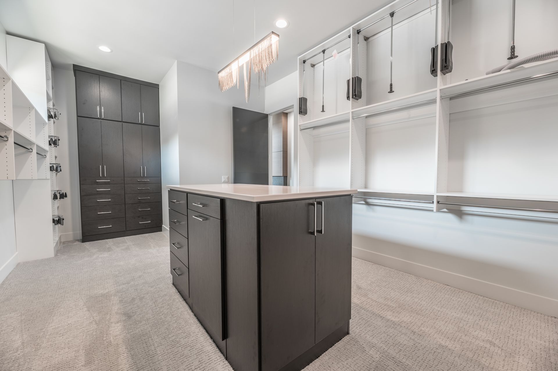 Spacious walk-in closet with dark cabinets, a central island, and white shelving. Carpeted floor, chandelier.