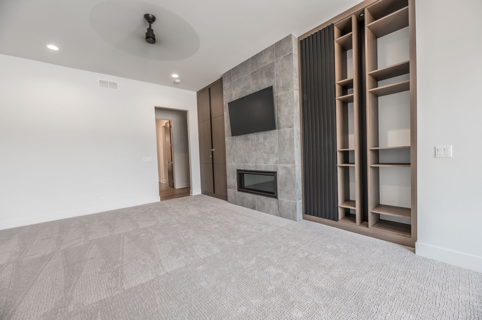 Spacious bedroom with gray carpet, built-in shelves, fireplace, and mounted TV on a gray stone wall.