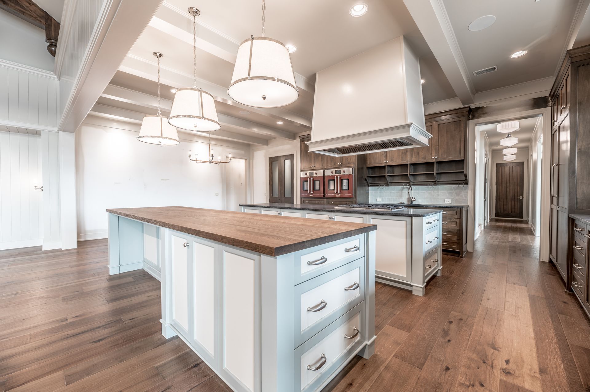 Spacious kitchen with wood floors, light blue cabinets, and wooden countertops. Overhead lights and range hood.