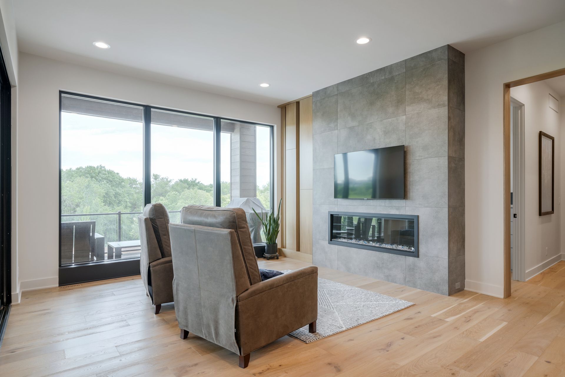 Living room with large window, fireplace, two armchairs, and light wood flooring.
