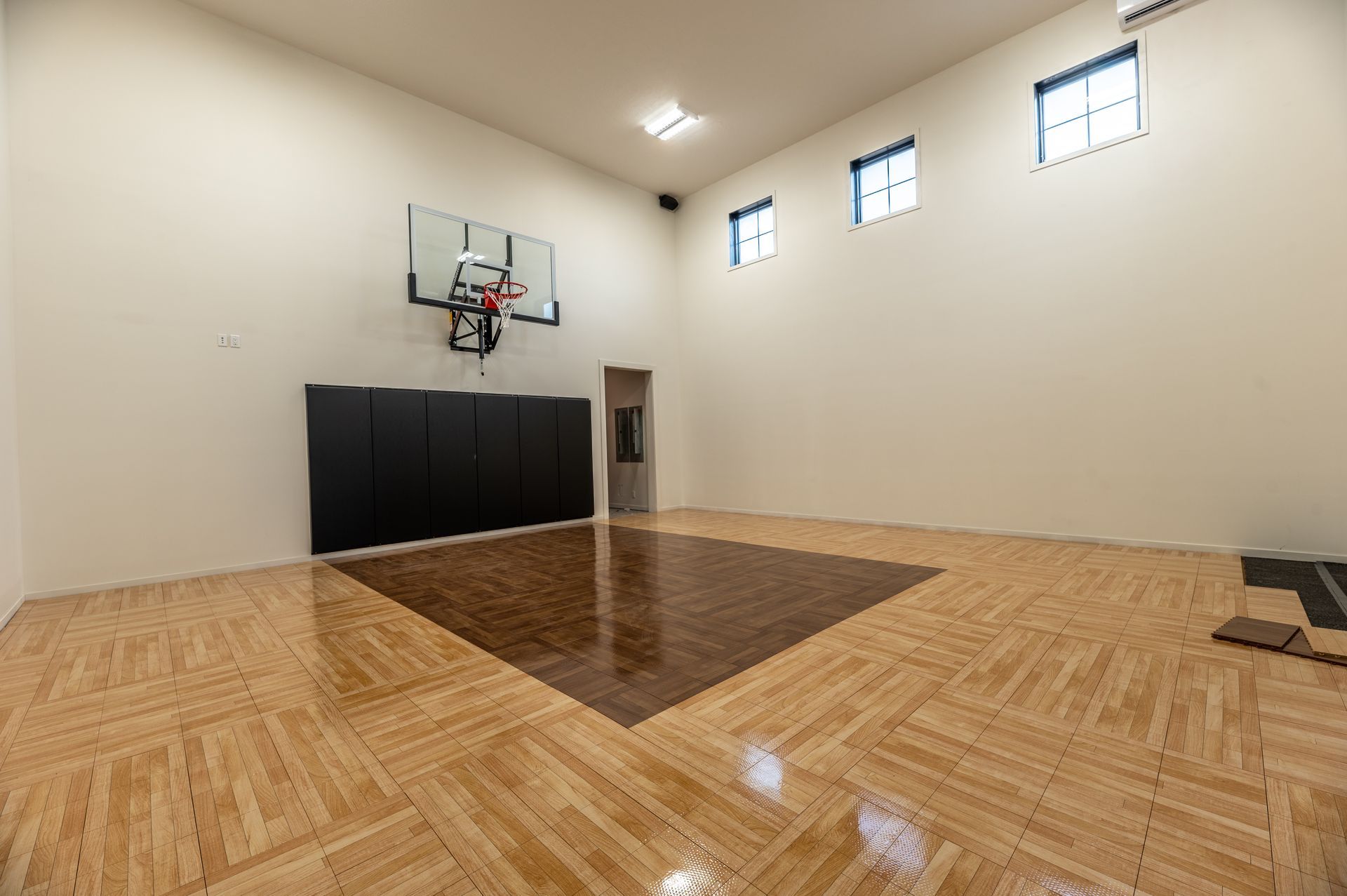 Empty indoor basketball court with wooden floors, hoop, and dark padded wall.