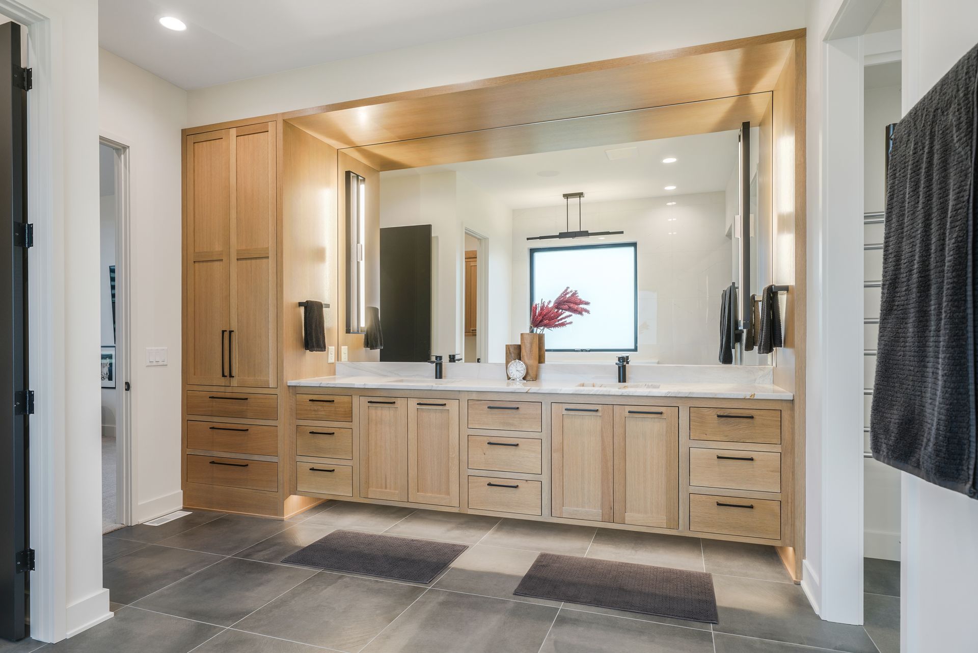 Modern bathroom with light wood cabinets, large mirror, and dark gray flooring.