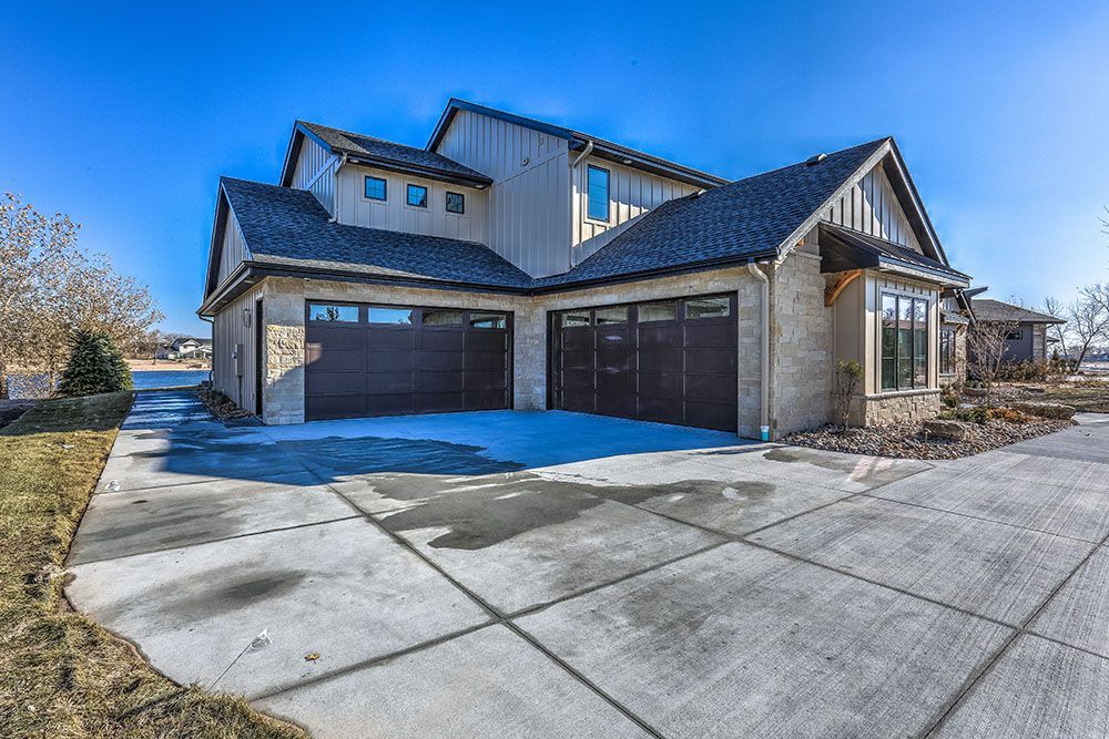 Modern two-story house with a three-car garage. Beige brick exterior, dark brown garage doors, and a blue sky.