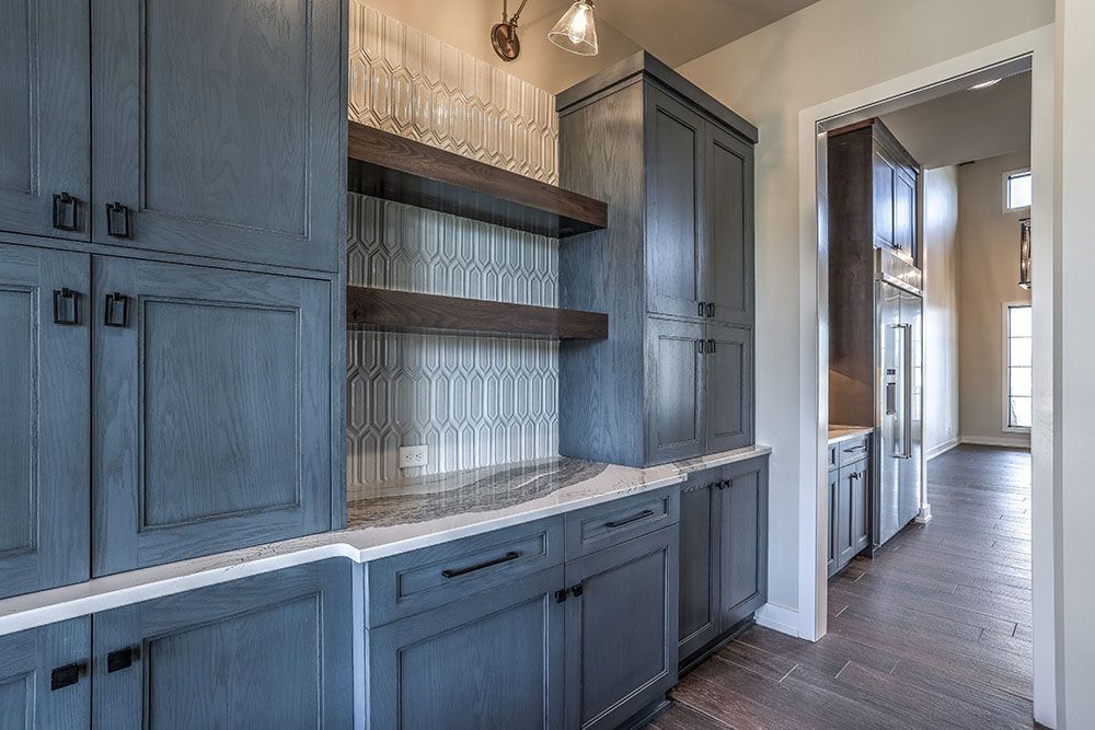 Blue kitchen cabinets with open shelving, tile backsplash, and dark wooden shelves.
