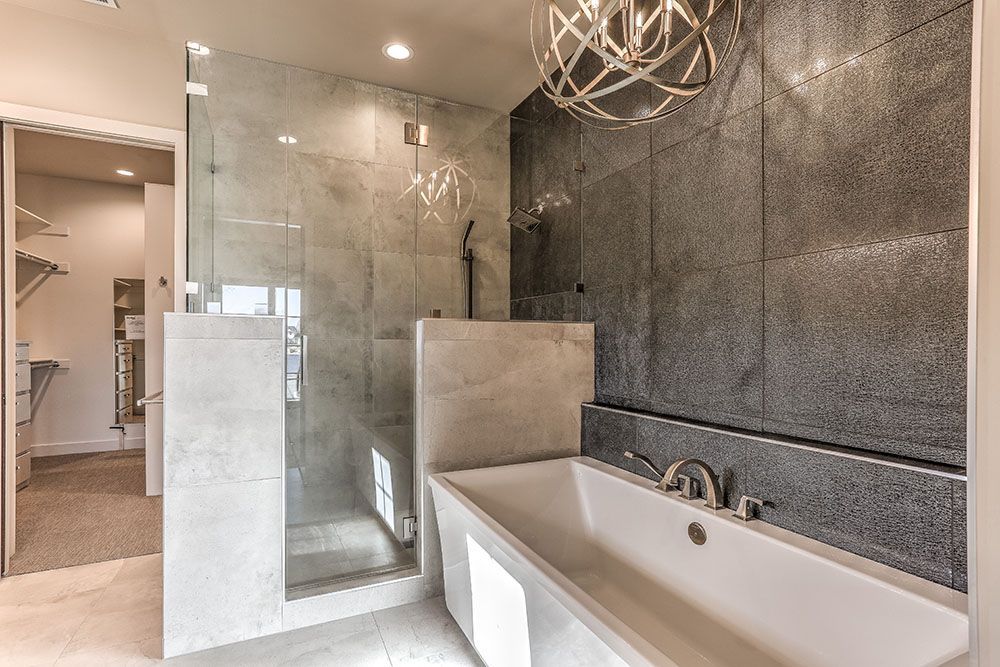 Modern bathroom with a glass shower, soaking tub, and gray tile accent wall.