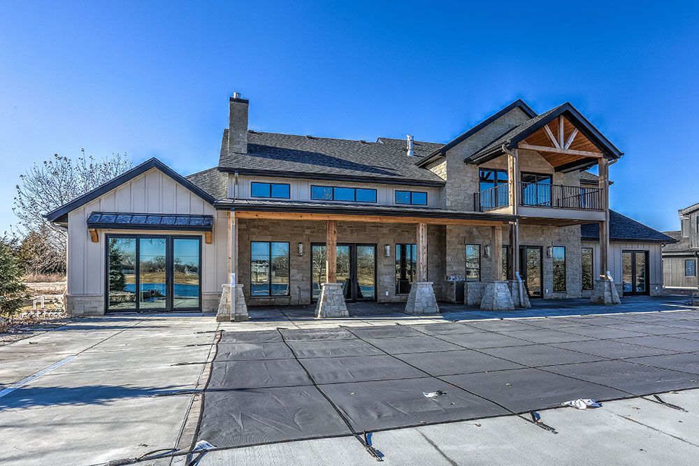 Luxurious stone house with a covered patio, balcony, and pool cover under a clear blue sky.