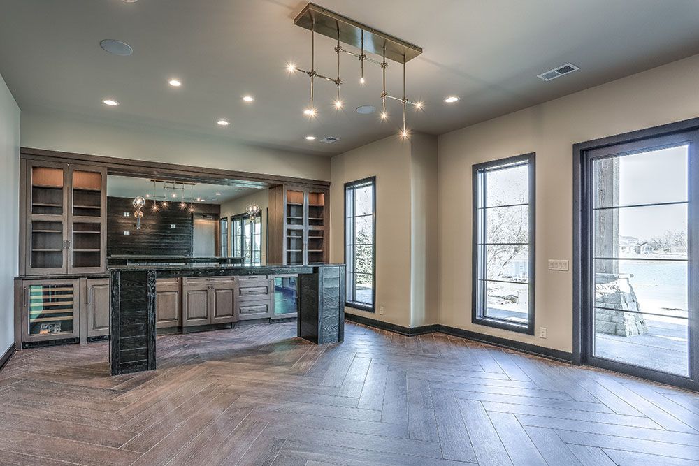 Empty room with bar, cabinets, windows. Gray walls, wood floor, modern light fixture.