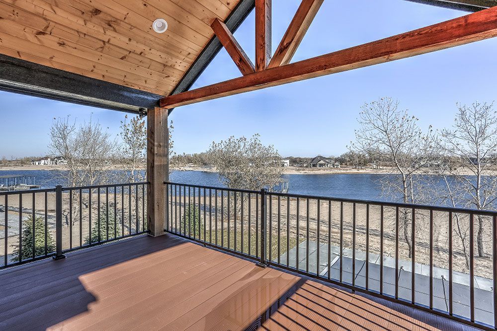Wooden deck overlooking a lake with a black railing, supporting beams, and a blue sky.