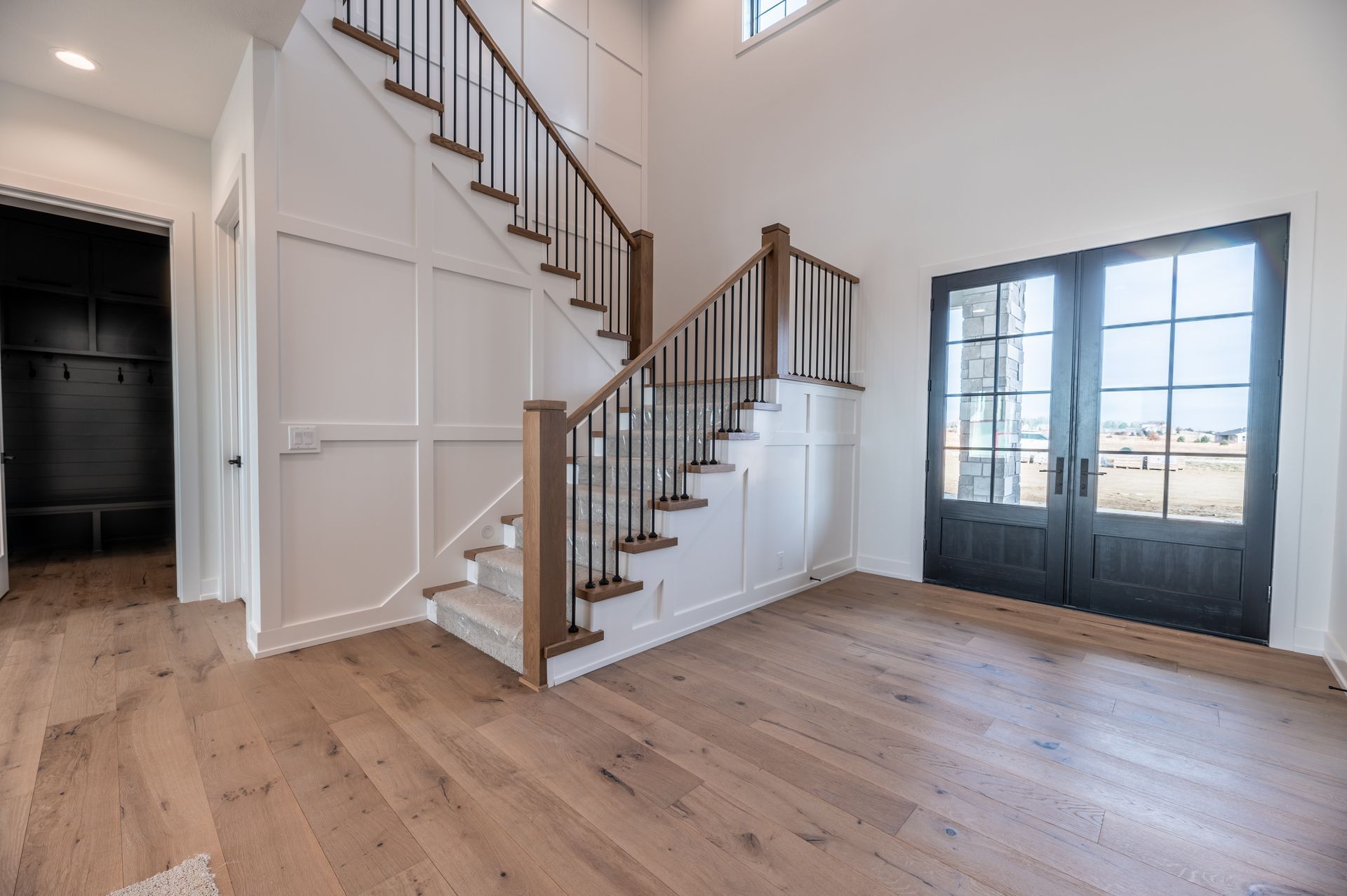 Open entryway with wooden floors, staircase, double doors, and white walls.