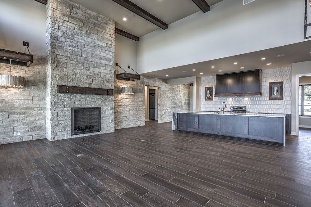 Spacious, modern kitchen with stone fireplace, dark wood floors, and gray cabinets.