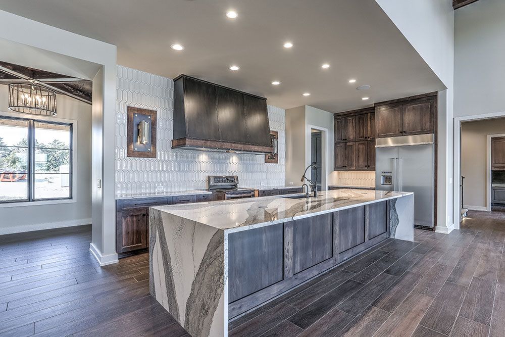 Modern kitchen with large island, dark cabinetry, light countertops, and hardwood floors.