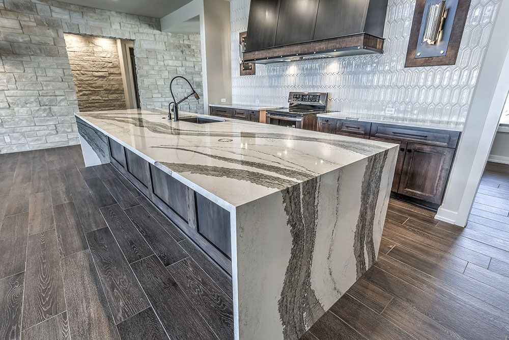 Modern kitchen with a large marble island, dark wood cabinets, and stone wall.