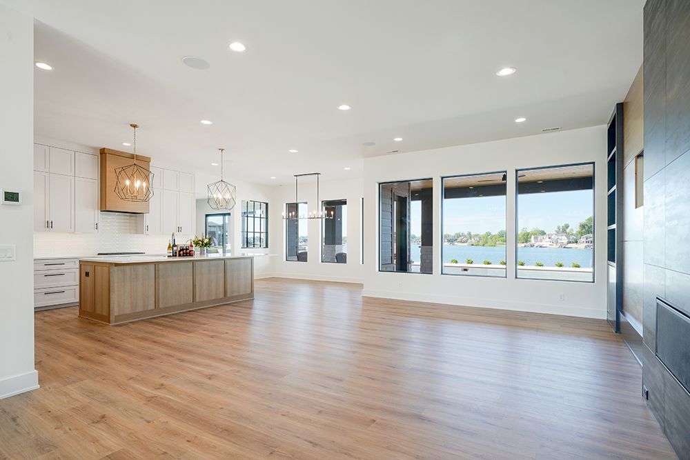 Spacious, modern interior with hardwood floors, a kitchen island, and large windows overlooking water.