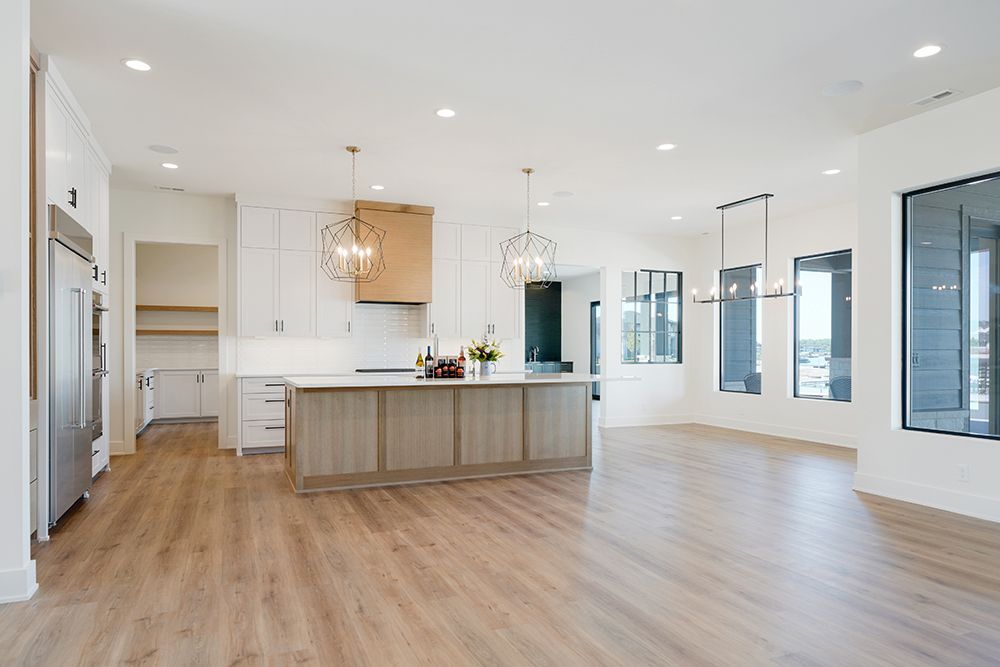 Open-concept kitchen with light wood floors, white cabinets, and a central island. Large windows provide natural light.