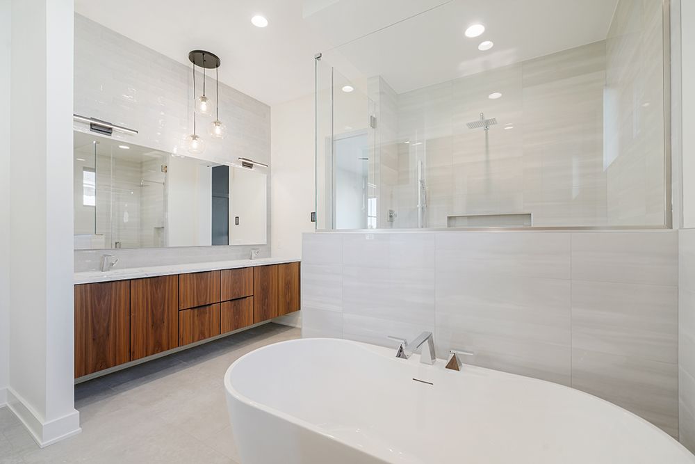 Modern white bathroom with wooden vanity, glass shower, and freestanding tub.