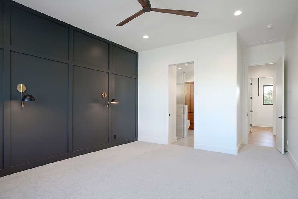 Bedroom with dark gray paneled wall, carpet, and an open door to a bathroom.