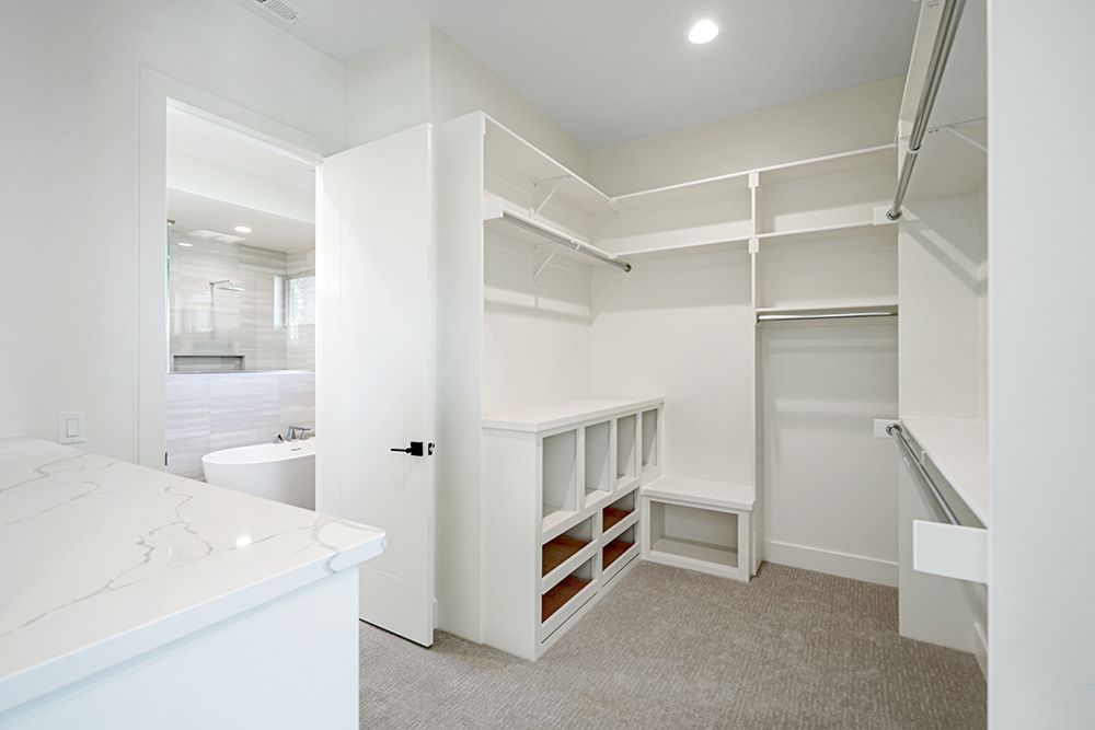Bright white walk-in closet with shelves, rods, and open doorway to a bathroom with a tub.