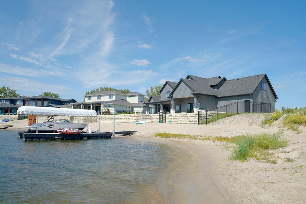 Beachfront houses with docks on a sunny day. Light sand, blue sky, and lake water.
