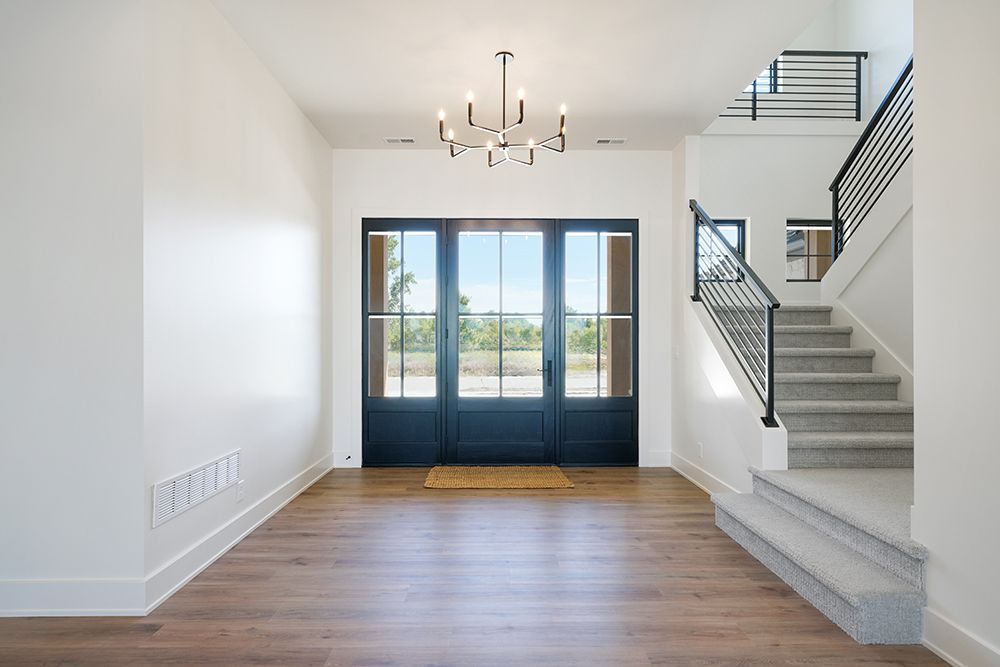 Entryway with dark blue doors, staircase, chandelier, and hardwood floors.