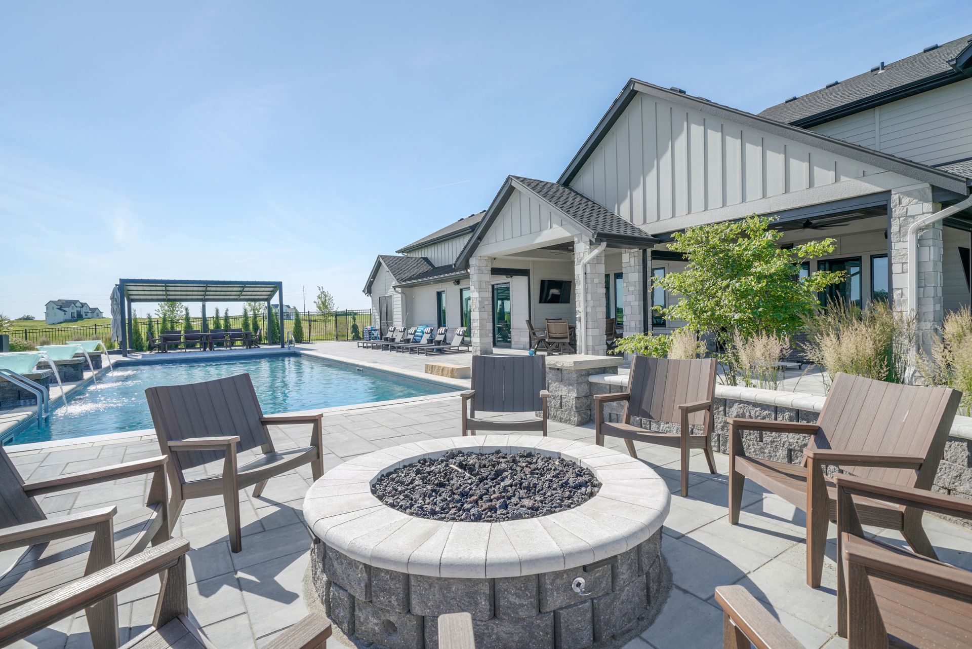 Backyard patio with fire pit, pool, and house on a sunny day.