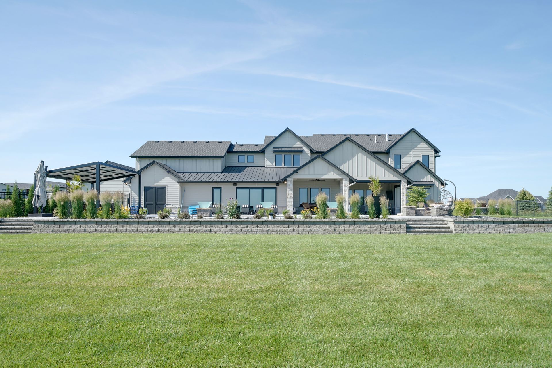 Large modern house with light siding, dark trim, and a manicured lawn under a blue sky.