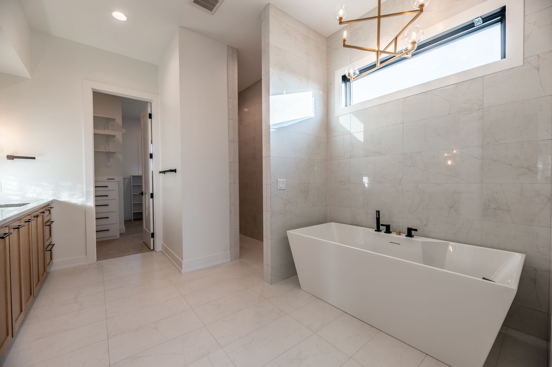 Modern bathroom with white soaking tub, light-colored tile, and wooden vanity.