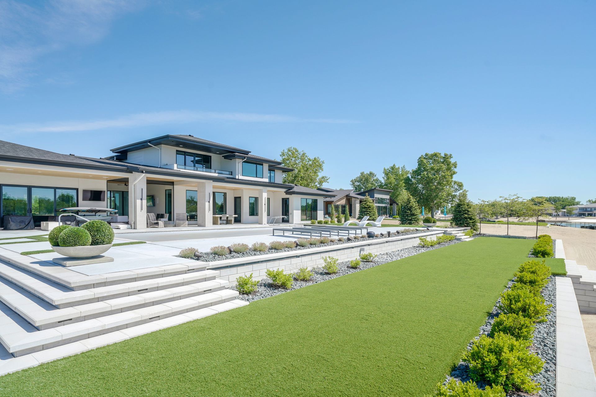 Luxury home exterior with patio, lawn, and landscaping under a blue sky.