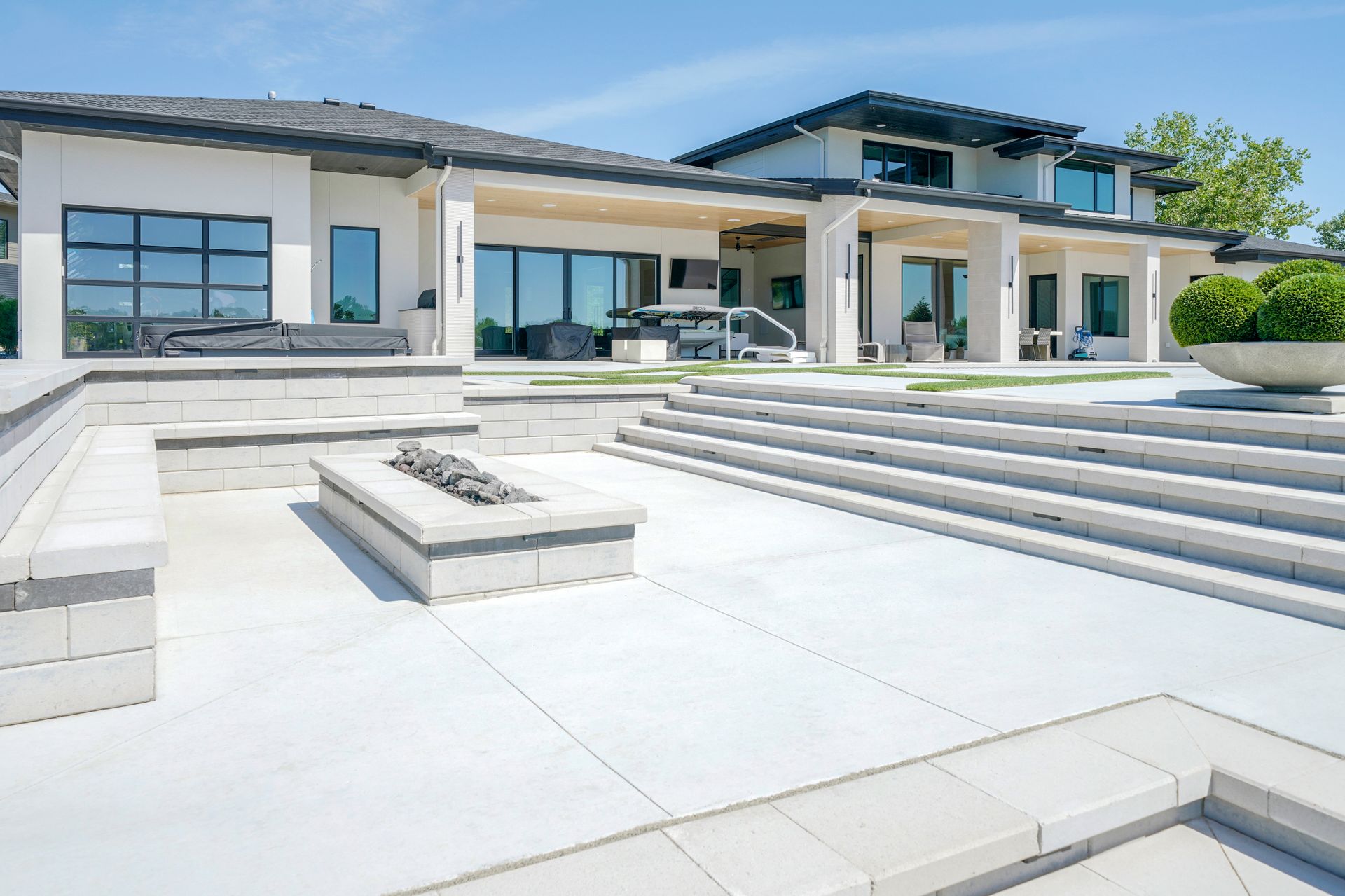 Modern white house with a patio, fire pit, and tiered seating on a sunny day.