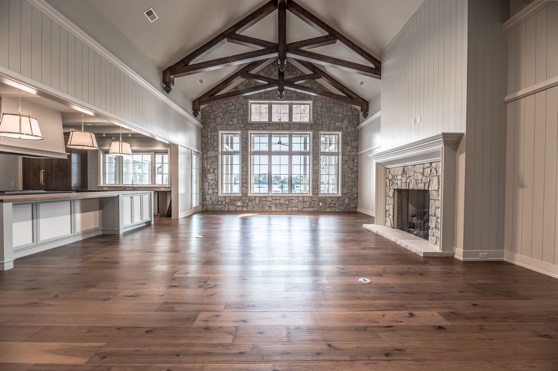 Spacious living room with wood floor, stone fireplace, large windows, and exposed wooden beams.