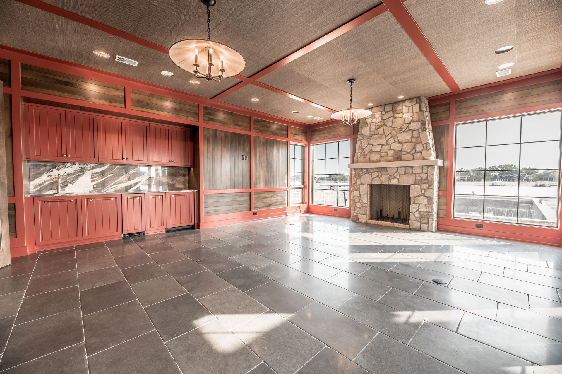 Spacious room with fireplace, cabinets, and large windows offering a waterfront view. Gray tiled floor, red accents.