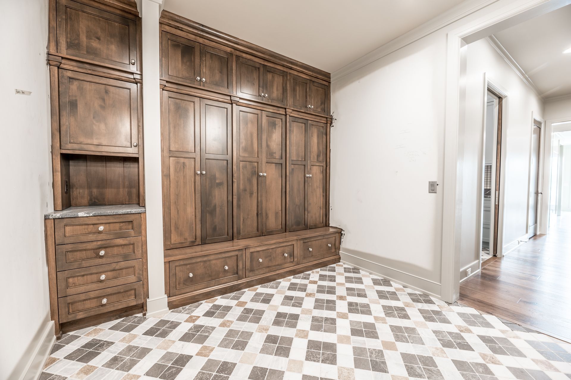 Wooden entryway storage cabinets with drawers and hanging hooks. Patterned tile floor. Hallway visible.