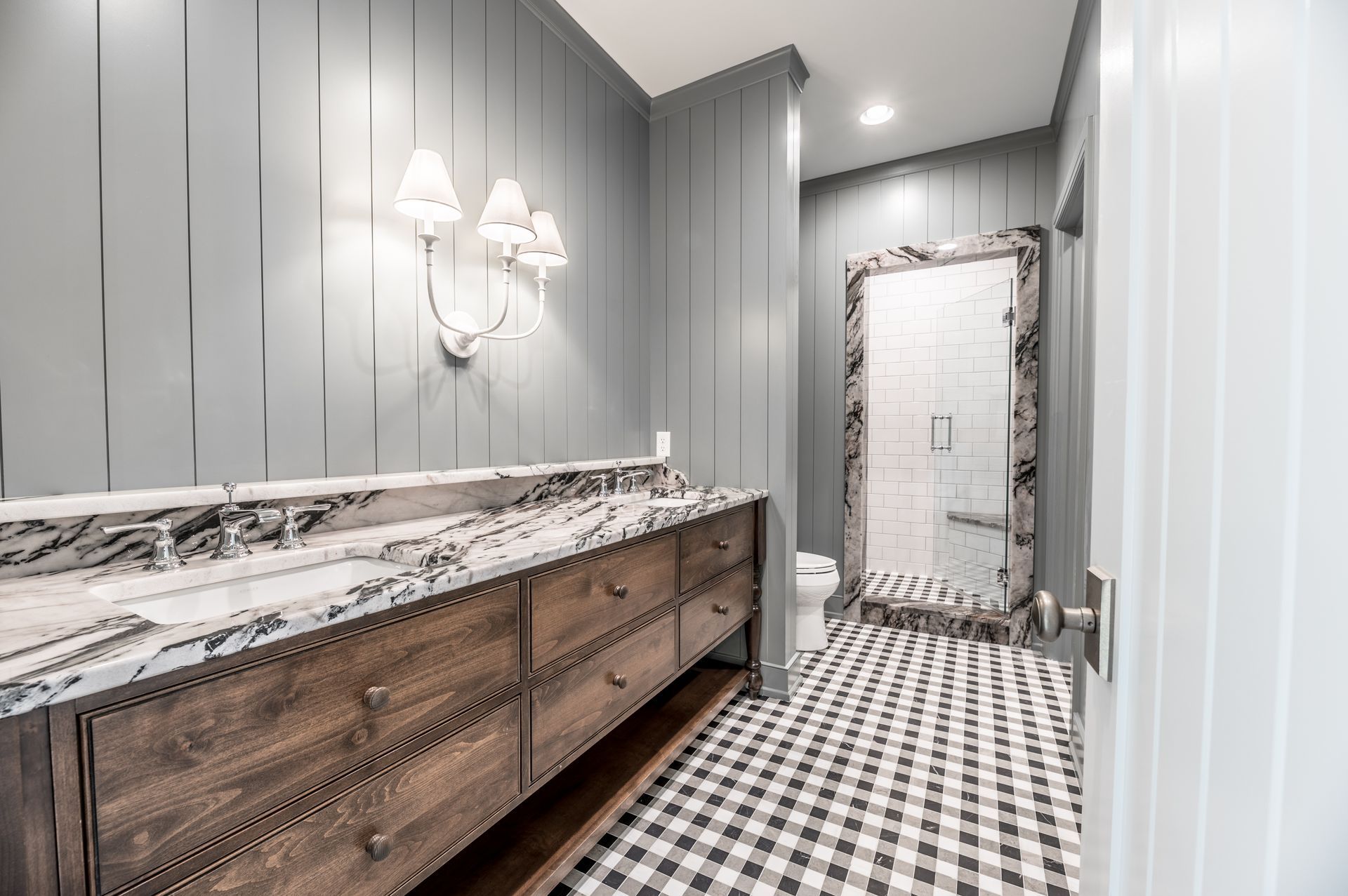 Bathroom with gray plank walls, checkered floor, marble vanity, and glass shower.