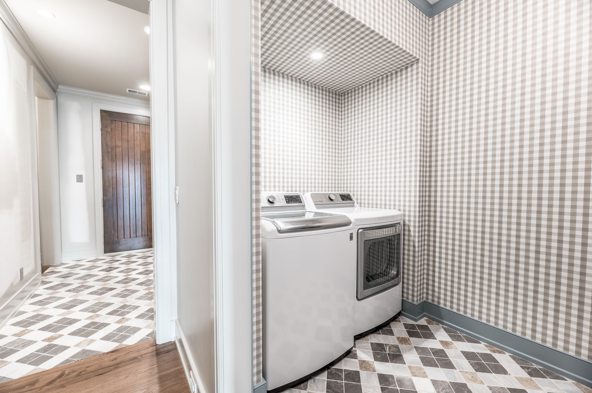 Laundry room with patterned wallpaper, washer, and dryer. Hallway with patterned floor.