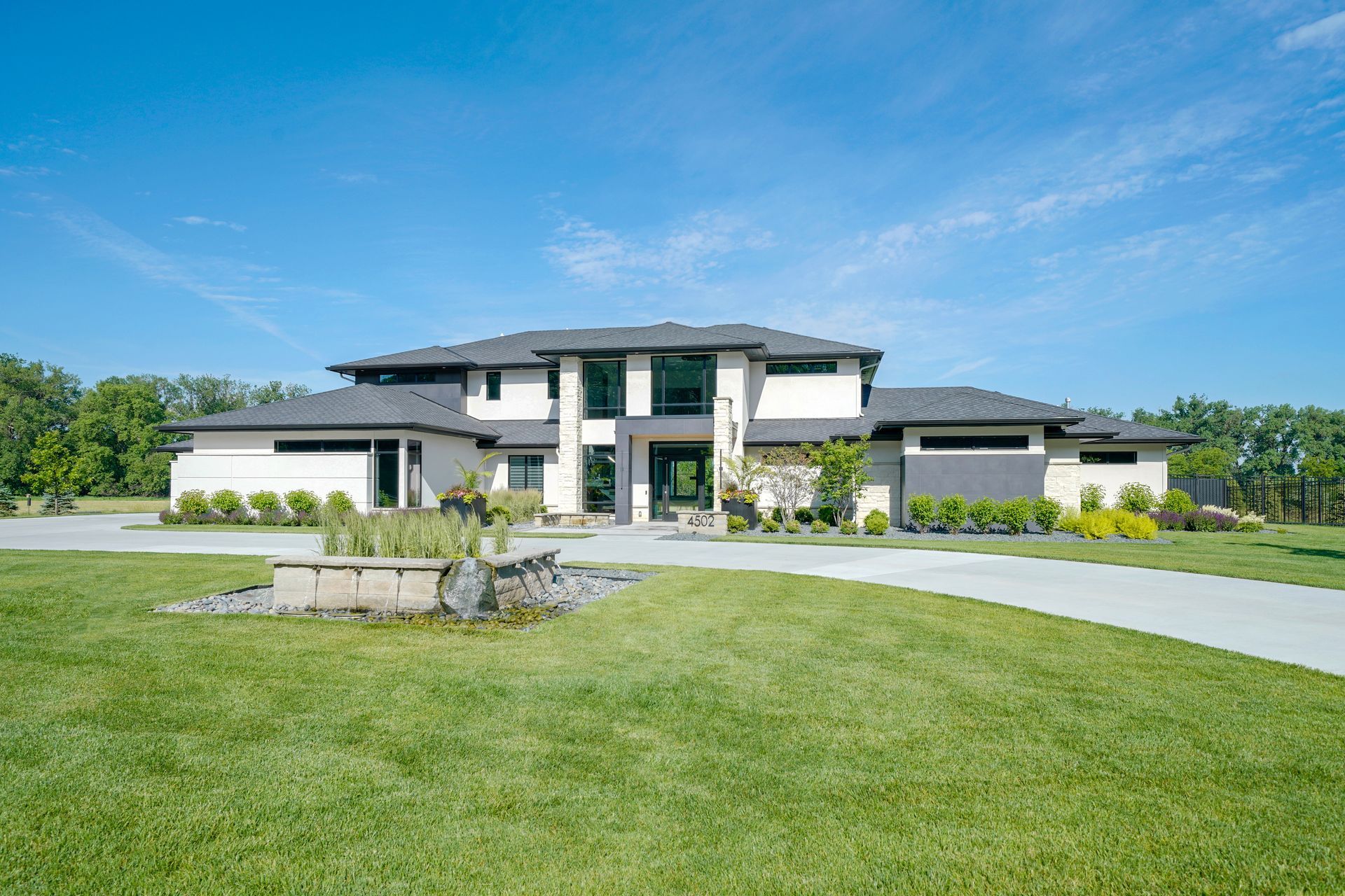 Modern two-story house with a long driveway and green lawn under a bright blue sky.